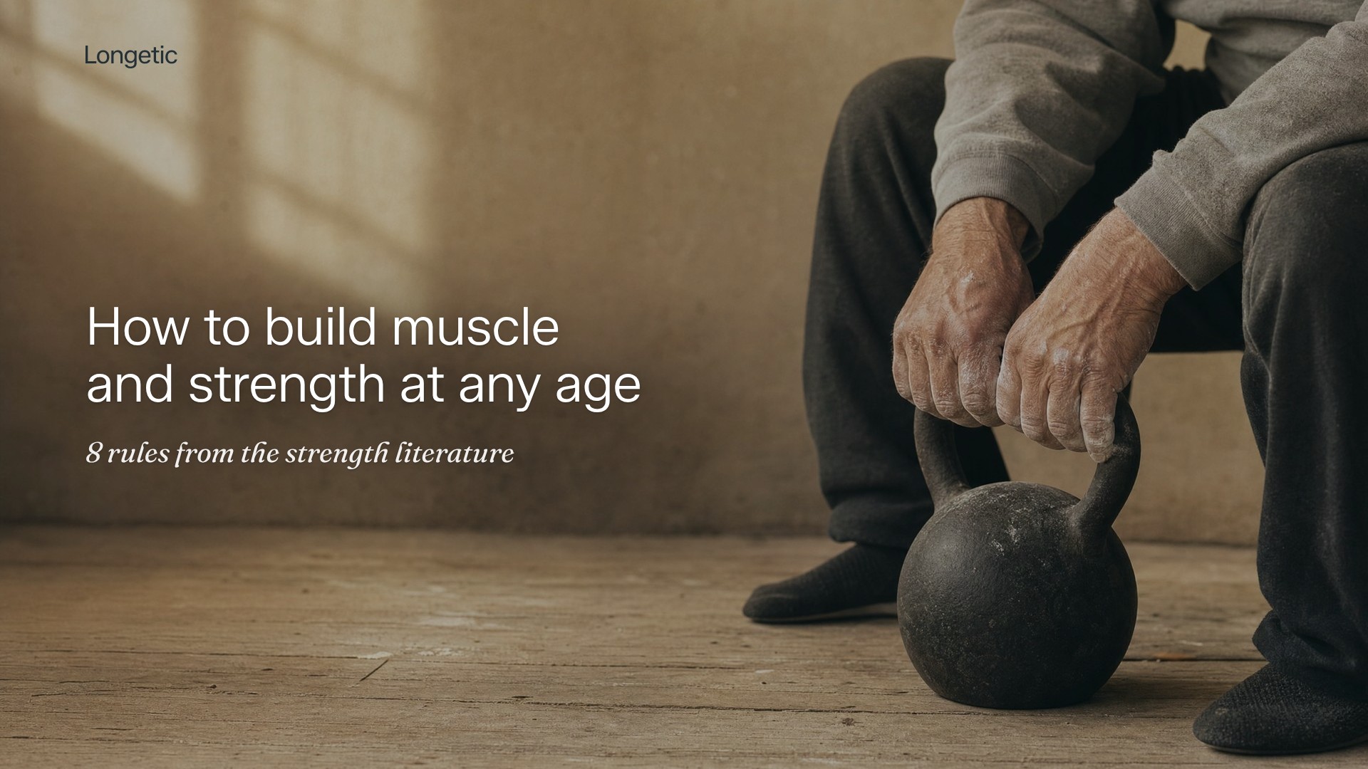 An older man in a grey sweatshirt sitting with both hands on the handle of a cast-iron kettlebell